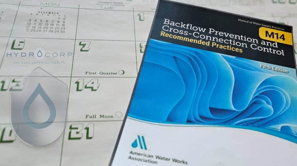 M14 manual on calendar with Hydro logo - Safeguarding Our Water: A Weeklong Journey Through Cross-Connection Control Programs | HydroCorp - HydroCorp